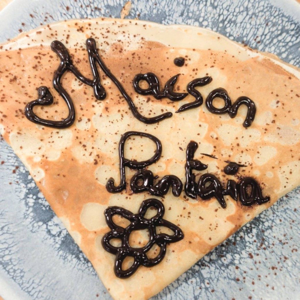 Une crêpe ornée du nom « Maison Pantaia » écrit au chocolat, avec une fleur